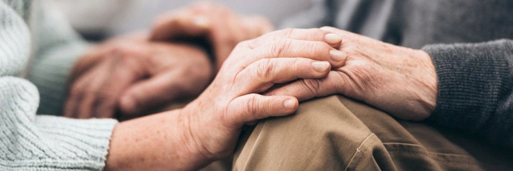 Senior citizen woman squatting down and placing hands senior man’s knees