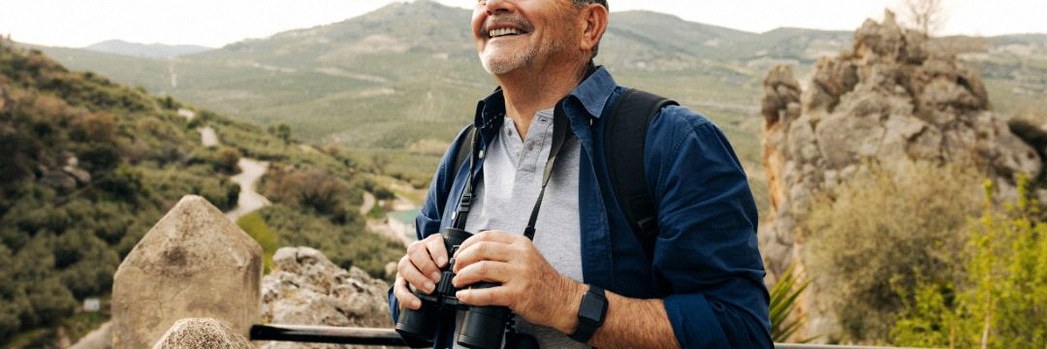 Older man in nature smiling holding binoculars