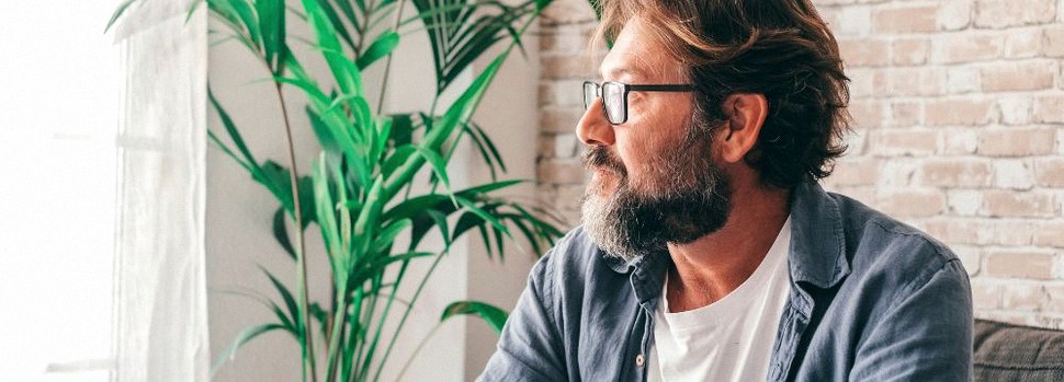 Middle age man with glasses looking out window on sunny day